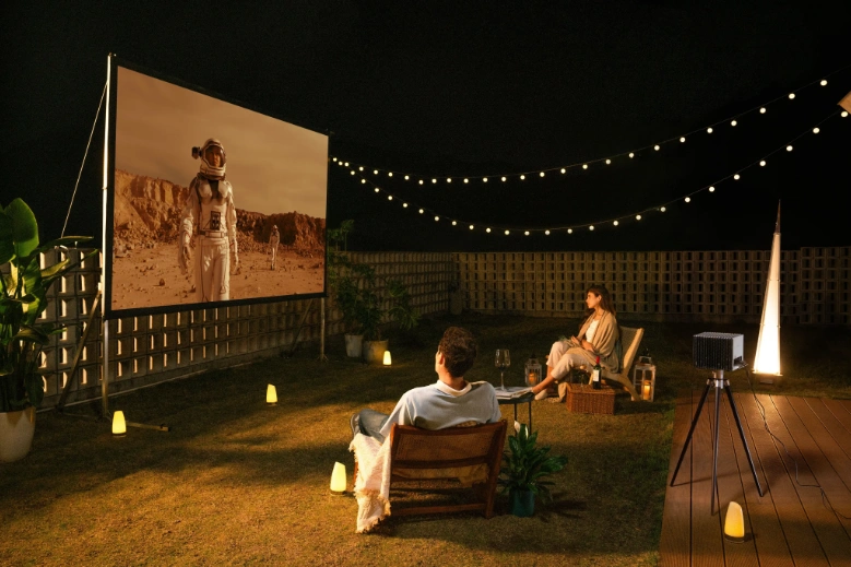 The family is enjoying a movie night with a projector and screen set up in their backyard.