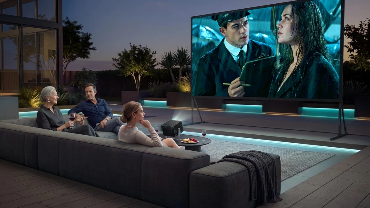 Trois personnes regardant un film en plein air sur une terrasse moderne avec un projecteur et un grand écran extérieur.